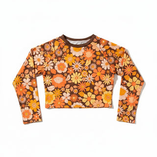A long-sleeve crop rash guard swim top featuring a retro 1970s floral pattern in orange, yellow, white, beige and brown background