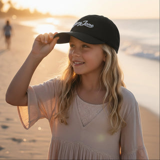 Young girl on a beach wearing a black cap with 'Berry Jane' branding.