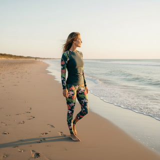 Woman standing on a beach wearing a full coverage UPF floral swim top with swim leggings